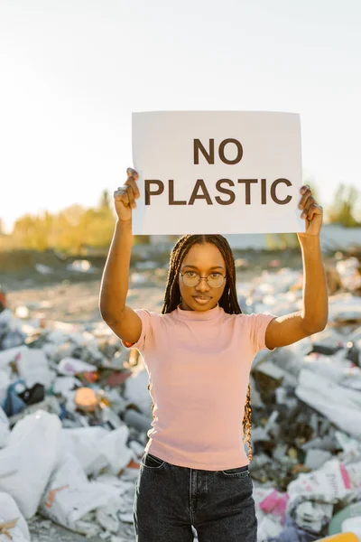 Young woman holding no plastic sign on trash place