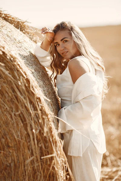 Beautiful young woman in vwhite dress sitting on hay bale. — Stock Photo, Image