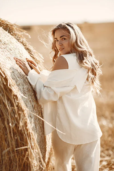 Beautiful young woman in vwhite dress sitting on hay bale. — Stock Photo, Image