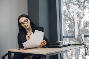 Ofisteki bir masada oturan ve belgeleri okuyan bir kadın..