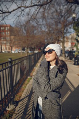 Kış şehrinde zarif bir kız yürüyor. Beyaz örgü kazaklı bir kadın. Koyu saçlı güzel bayan..