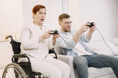 Kıdemli engelli kadın oğluyla video oyunu oynuyor.