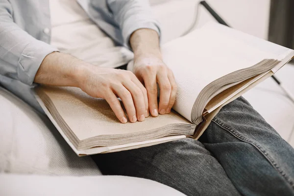 Сліпий молодий чоловік читає книгу брайля на дивані — стокове фото
