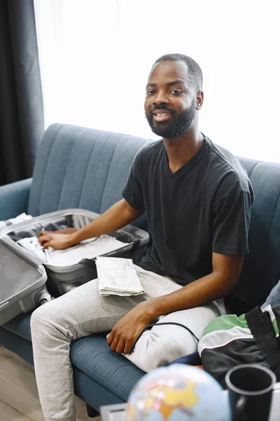 Afrikaner sitzt auf einem Sofa und packt sein Gepäck — Stockfoto