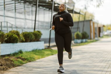 Afro-Amerikan artı boyunda kadın dışarıda koşuyor.