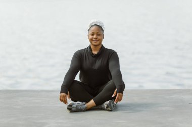Afro-Amerikalı ve iri yarı kadın dışarıda yoga yapıyor.