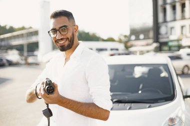 Arab man holding electric car plug. Smiling at camera, standing in the city near electro car.