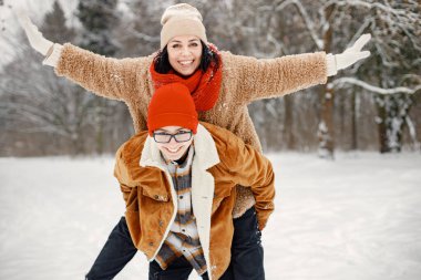 Oğlu annesini sırtında taşıyor. Neşeli çocuk ve güzel annesi kış parkında birlikte vakit geçiriyorlar. Sıcak ceket ve kırmızı kazak giyen bir kadın..