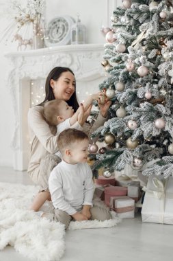 Anne ve iki oğlu Noel ağacı süslüyorlar. Noel 'de heyecanlı bir aile. Beyaz elbiseli bir kadın ve iki çocuk..