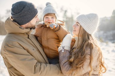 Mutlu aile portresi kış yürüyüşünde eğleniyor ve sarılıyor. Zencefilli çörek tutan küçük bir çocuk. Aile ceketi ve örgü şapkalar giyiyor..