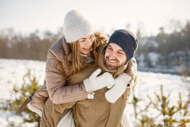 Kış yürüyüşünde eğlenen romantik çift portresi. Kadını sırtında taşıyan bir adam. Aile ceketi ve örgü şapkalar giyiyor..