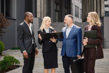 Modern ofis binasının önünde duran kendinden emin iş adamları. Erkekler ve kadınlar ellerinde belgelerle konuşuyor. Bankacılık ve finans piyasası kavramı.