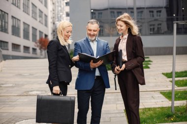 Modern ofis binasının önünde duran kendinden emin iş adamları. Kadın ve erkek konuşuyor ve ellerinde belgeler var. Bankacılık ve finans piyasası kavramı.