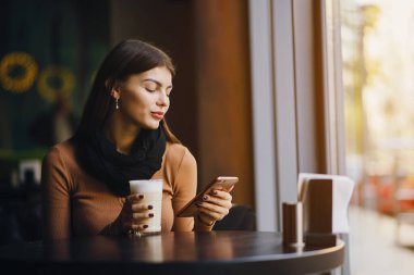 Esmer kız restoranda kahve içerken telefonunu kullanıyor.