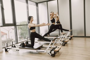 Three young fit women training in gym. Women wearing black sportwears. Caucasian girls excercising with equipment.