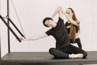 Young fit woman with a female trainer in gym. Woman wearing black sportwear. Caucasian girl stretching with equipment.