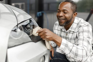 Man washing luxury car on a car wash with a rag. Black man wiping his car. Man wearing plaid shirt, smiling.