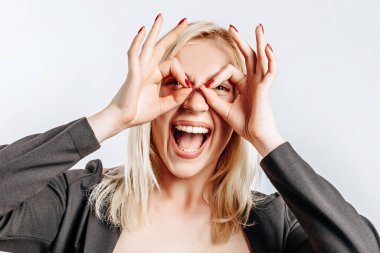 Güzel, genç, tatlı bir kız, gülümsüyor. Gri, izole arka planda aptalca hareketler yapıyor.