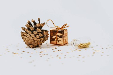 Altın ve gümüş bilezikler şişelerden, hediyelerden, köknar konilerinden ve beyaz arka planda bir hediyeden dağılır.