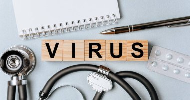 Wooden block form the word VIRUS with stethoscope, pills, notepad, pen on the doctor's desktop. Medical concept.