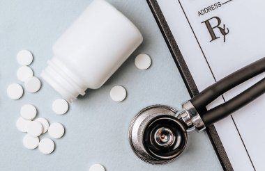 Beyaz haplar, steteskop, doktorun masasında reçete. Tıp konsepti. Tıbbi ürünlerin dozunu belirleme araştırması. Sağlık hizmeti ya da hastalık. Hastanede veya eczanede hap veya hap.