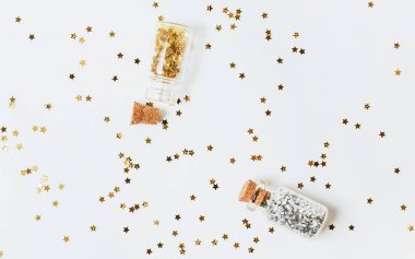Spangles of gold and silver are scattered from bottles on a white background clipart