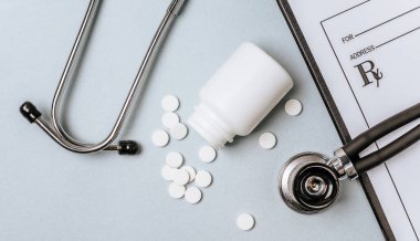 Beyaz haplar, steteskop, doktorun masasında reçete. Tıp konsepti. Tıbbi ürünlerin dozunu belirleme araştırması. Sağlık hizmeti ya da hastalık. Hastanede veya eczanede hap veya hap.