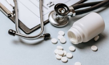 Beyaz haplar, steteskop, doktorun masasında reçete. Tıp konsepti. Tıbbi ürünlerin dozunu belirleme araştırması. Sağlık hizmeti ya da hastalık. Hastanede veya eczanede hap veya hap.