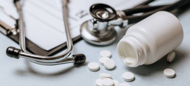 Beyaz haplar, steteskop, doktorun masasında reçete. Tıp konsepti. Tıbbi ürünlerin dozunu belirleme araştırması. Sağlık hizmeti ya da hastalık. Hastanede veya eczanede hap veya hap.