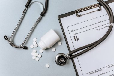 Beyaz haplar, steteskop, doktorun masasında reçete. Tıp konsepti. Tıbbi ürünlerin dozunu belirleme araştırması. Sağlık hizmeti ya da hastalık. Hastanede veya eczanede hap veya hap.