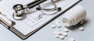 Beyaz haplar, steteskop, doktorun masasında reçete. Tıp konsepti. Tıbbi ürünlerin dozunu belirleme araştırması. Sağlık hizmeti ya da hastalık. Hastanede veya eczanede hap veya hap.