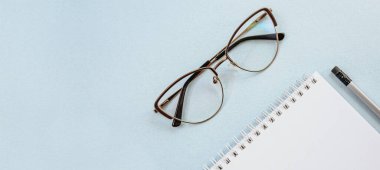 Ofis kavramı. Çalışma alanı gözlüklü, defterli ve kalemli. Boşluğu beyaz ve mavi olarak kopyala.