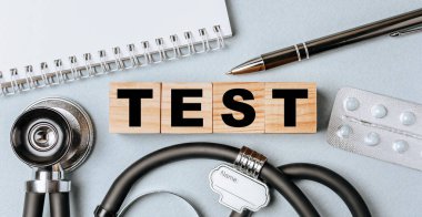 Wooden block form the word TEST with stethoscope, pills, notepad, pen on the doctor's desktop. Medical concept.