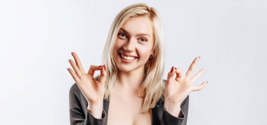 Güzel, genç, mutlu bir kız, güzel bir jest yapıyor ve gri arka planda gülümsüyor.