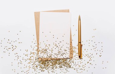 Beyaz arkaplanda boş bir not, kalem ve altın parıltılı yıldızlar