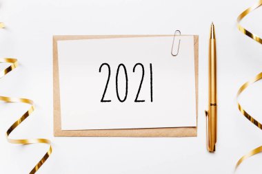 Zarf, kalem, hediyeler ve beyaz arka planda altın kurdeleyle 2021 yılına ait bir not. Mutlu Noeller ve yeni yıl konsepti