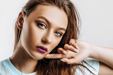 Güzel, genç, esmer, yeşil gözlü, uzun saçlı, moda makyajlı, mor dudaklı, izole gri arka planda bir kız. Kadın el ele tutuşup ciddi ciddi kameraya bakıyor..