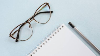 Ofis kavramı. Çalışma alanı gözlüklü, defterli ve kalemli. Boşluğu beyaz ve mavi olarak kopyala.