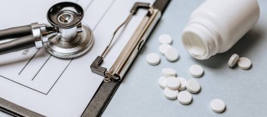 Beyaz haplar, steteskop, doktorun masasında reçete. Tıp konsepti. Tıbbi ürünlerin dozunu belirleme araştırması. Sağlık hizmeti ya da hastalık. Hastanede veya eczanede hap veya hap.