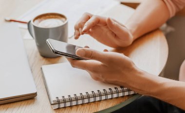 Adam iş yerindeki not defterine akıllı telefonuyla iş bilgileri yazıyor.