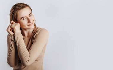 Genç güzel esmer kız gülümsüyor ve dokunuyor ve beyaz tenha bir arkaplanda iki elini tutuyor.