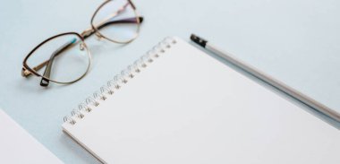 Ofis kavramı. Çalışma alanı gözlüklü, defterli ve kalemli. Boşluğu beyaz ve mavi olarak kopyala.