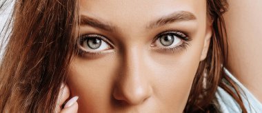 Güzel, tatlı, esmer, yeşil gözlü, uzun saçlı, moda makyajlı, izole gri arka planda bir kız. Kadın elini yüzüne dayadı ve kameraya baktı. Hoş bir model.