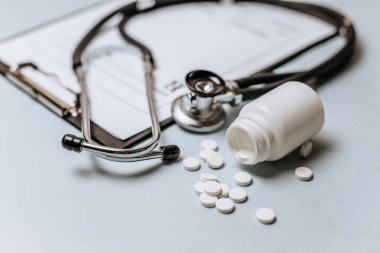 Beyaz haplar, steteskop, doktorun masasında reçete. Tıp konsepti. Tıbbi ürünlerin dozunu belirleme araştırması. Sağlık hizmeti ya da hastalık. Hastanede veya eczanede hap veya hap.