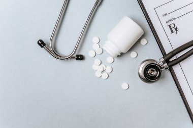 Beyaz haplar, steteskop, doktorun masasında reçete. Tıp konsepti. Tıbbi ürünlerin dozunu belirleme araştırması. Sağlık hizmeti ya da hastalık. Hastanede veya eczanede hap veya hap.