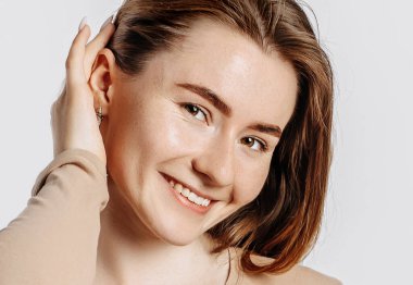 Güzel, genç esmer kadın gülümseyen ve poz veren beyaz izole bir arka planda kameraya bakıyor.