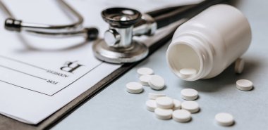 Beyaz haplar, steteskop, doktorun masasında reçete. Tıp konsepti. Tıbbi ürünlerin dozunu belirleme araştırması. Sağlık hizmeti ya da hastalık. Hastanede veya eczanede hap veya hap.