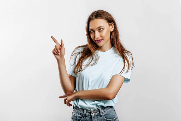 Portrait of a smiling girl pointing finger to the side at on a white isolated background. A woman points to an idea, a place for advertising. Positive girl with fashion make-up with purple lips.