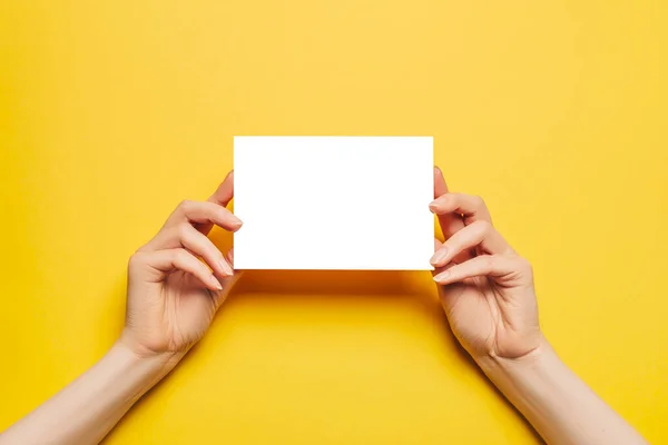 女性的手拿着一张黄色背景的空白纸片 广告空间 — 图库照片