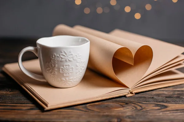 Heart made from book sheets with a cup, love and valentine concept on a wooden table